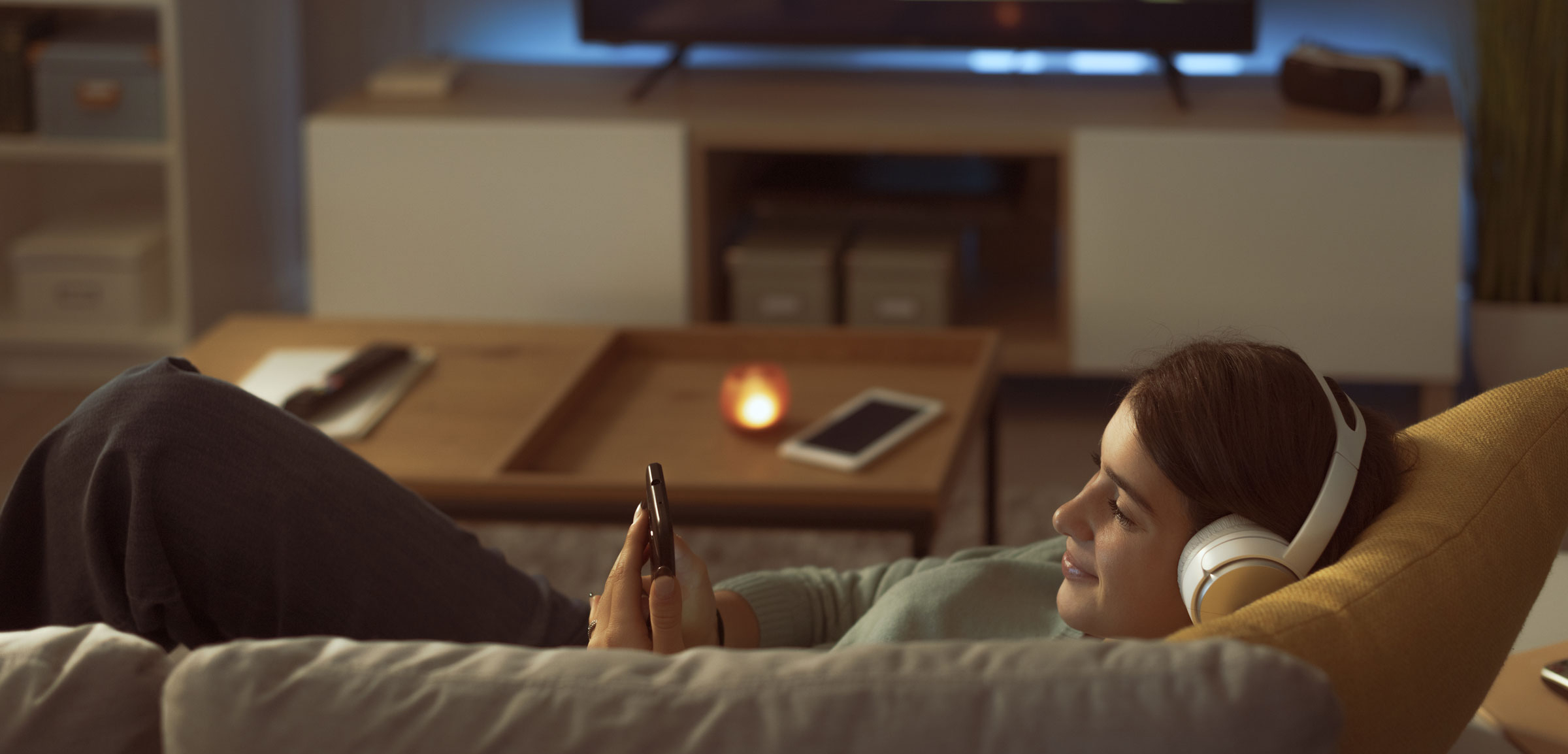 Teenager relaxing on the sofa in the living room, she is wearing headphones and connecting online with her smartphone
