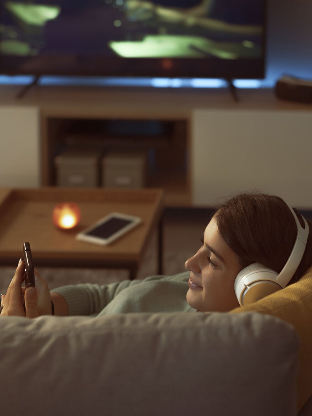 Teenager relaxing on the sofa in the living room, she is wearing headphones and connecting online with her smartphone